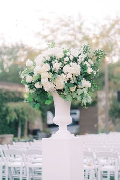 a tall white vase filled with flowers on top of a table covered in white chairs