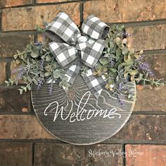 a welcome sign hanging on the side of a brick wall with flowers and greenery