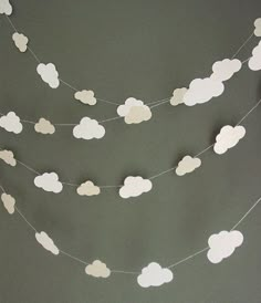 paper clouds are hanging from a string on the wall in front of a gray background