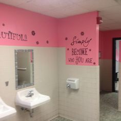 a pink and white bathroom with two sinks, mirror and urinals on the wall