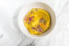 a white bowl filled with yellow food on top of a marble counter next to a knife and fork