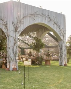 an outdoor wedding venue set up with white drapes and tables covered in flowers on the grass