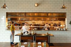 two people standing in front of a counter with pots and pans on top of it