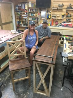 two people sitting at a wooden table in a shop with workbench and tools