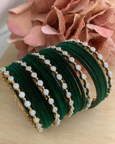 four green bangles with white stones on them next to pink flowers and a bouquet