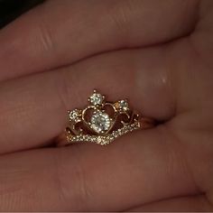 a woman's hand holding a gold ring with a diamond in the middle and a crown on top