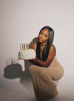 a woman kneeling down holding a cake with candles on it in front of her face