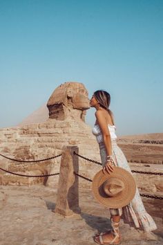 a woman in a white dress and straw hat standing next to the sphinx at giza