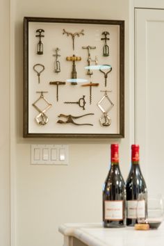 two bottles of wine sitting on top of a counter next to a wall mounted corkscrews