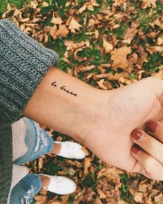 two people holding hands with the word love tattooed on their wrist, in front of leaves