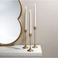 three candles are on a table next to a mirror and a gold framed round mirror