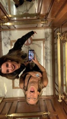 two women standing in front of a mirror taking a selfie with their cell phone