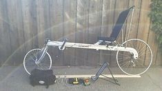 a bicycle parked next to a wooden fence with a bag on the ground beside it