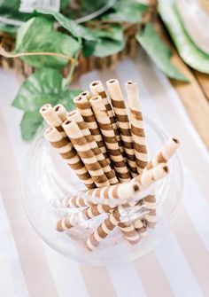 striped paper straws in a glass bowl on a table with greenery behind them