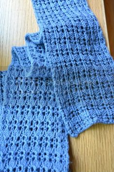 two blue crocheted pieces of cloth sitting on top of a wooden table next to each other