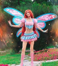 a woman in a pink and blue fairy costume standing on a brick walkway with her arms outstretched