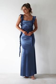 a woman in a blue dress is standing with her hands on her hips and looking down