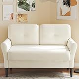 a white couch sitting on top of a wooden floor next to a wall filled with pictures