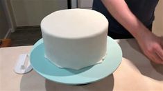 a person is decorating a white cake on a table with blue plates and utensils