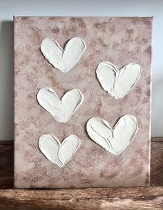 four white heart shaped cookies sitting on top of a wooden table next to a wall