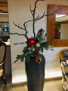 a black vase filled with pine cones and greenery sitting on top of a tiled floor