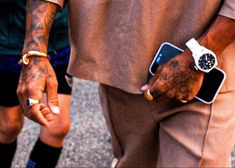 two people holding hands with tattoos on their arms and one has a cell phone in his other hand