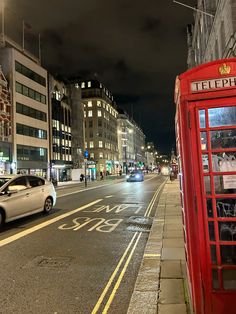 a red telephone booth sitting on the side of a road next to a white car