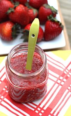 a jar of strawberry jam sitting on top of a table next to some strawberries