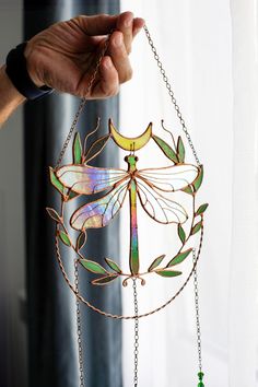 a hand holding a dragonfly wind chime hanging from a chain