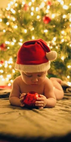 a baby wearing a santa hat on top of a bed next to a christmas tree