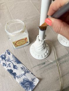 someone is using a brush to paint the top of a candle holder with blue and white flowers