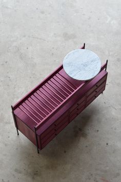 a red bench with a marble top on it's legs and two drawers underneath