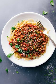 a white plate topped with spaghetti and meat sauce next to a fork on top of a table