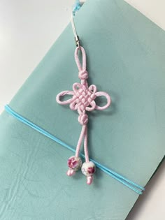 a pink crocheted cross hanging from a blue string on top of a piece of paper