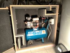 a small blue air compressor in a wooden box with wheels on the floor and other items inside