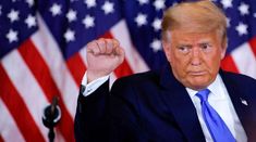 a man in a suit and tie raising his fist with an american flag behind him