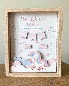 a wooden frame with a pink and blue unicorn on it's side, hanging from the wall