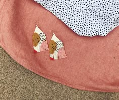 two pairs of earrings sitting on top of a pink cushion next to a polka dot pillow