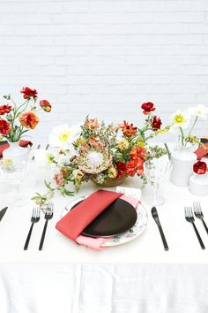 the table is set with red and white plates, silverware, and flower arrangements