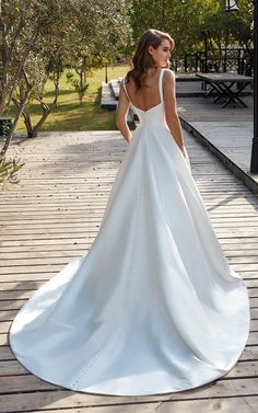 a woman in a white wedding dress is standing on a wooden deck with her back to the camera