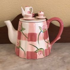 a pink and white checkered tea pot with two cups sitting on top of it