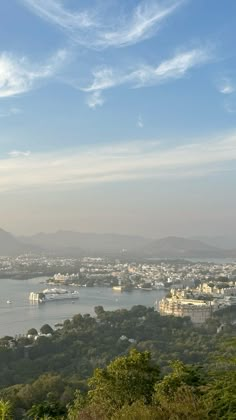 the city is surrounded by trees and mountains, with water in the foreground as far as the eye can see