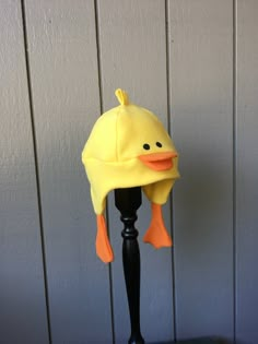 a yellow ducky hat on top of a black pole next to a white wall