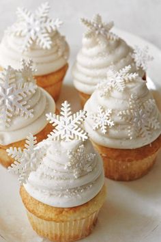 four cupcakes with white frosting and snowflakes on top are sitting on a plate