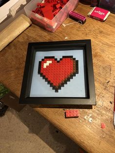 a red heart in a black frame sitting on top of a table next to some legos