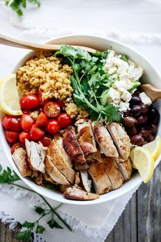 a white bowl filled with chicken, tomatoes, olives, rice and garnishes