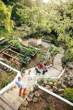 two children are walking up some steps in a garden with trees and plants on the other side