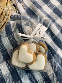 some heart shaped cookies wrapped in plastic on a checkered tablecloth with a basket behind them