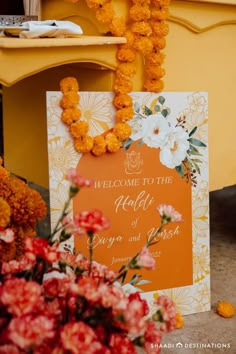 an orange welcome sign surrounded by flowers