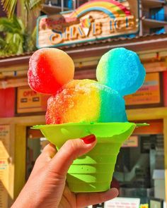 someone holding up a mickey mouse ice cream cone in front of a disney world store